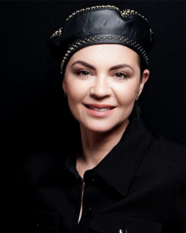 Architekt wnętrz Anna Buczny z pracowni Anna Buczny Piękne Wnętrza w Szczecinie. Zdjęcie jest utrzymane w kolorystyce ciemnego tła z rozświetloną twarzą uśmiechającej się projektantki.