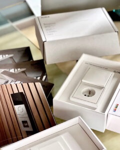 Osprzęt elektryczny Gira kolekcja F-100 w kolorze białym w formie próbek. Katalogi firmy Gira. Całość wyłożona na szklanym stole w pracowni projektowej Anna Buczny Piękne Wnętrza.