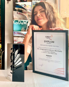 Szczecińska architekt wnętrz Anna Buczny z pracowni Anna Buczny Piękne Wnętrza, siedzi przy stoliku w jednej ze szczecińskich restauracji, z dyplomem i nagrodą, uzyskaną w konkursie Orły wnętrz 2025, z najwyższą oceną 10/10 punktów. Tak wysoką ocenę szczecińska projektantka uzyskana na podstawie opinii Klientów. Tym samym Anna Buczny została najlepszym projektantem i architektem wnętrz w szczecinie i województwie zachodniopomorskim roku 2025.