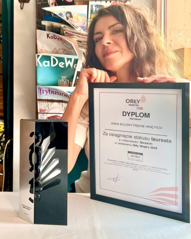 Szczecińska architekt wnętrz Anna Buczny z pracowni Anna Buczny Piękne Wnętrza, siedzi przy stoliku w jednej ze szczecińskich restauracji, z dyplomem i nagrodą, uzyskaną w konkursie Orły wnętrz 2025, z najwyższą oceną 10/10 punktów. Tak wysoką ocenę szczecińska projektantka uzyskana na podstawie opinii Klientów. Tym samym Anna Buczny została najlepszym projektantem i architektem wnętrz w szczecinie i województwie zachodniopomorskim roku 2025.