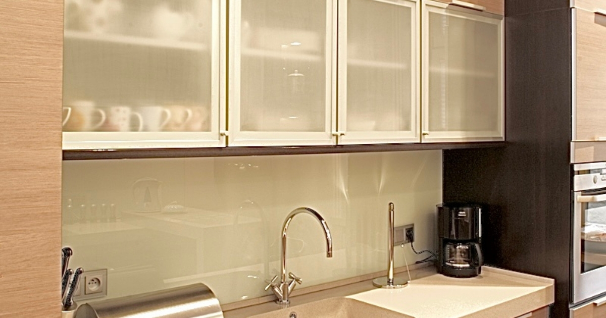 Meble kuchenne wykonane na zamówienie, według projektu architekt wnętrz Anny Buczny. Proste, nowoczesne fronty szafek, utrzymane są w ciepłej kolorystyce, imitują drewno. Pomiędzy wysokimi szafkami o głębokości 60 cm, znajdują się wiszące witrynki z frontami szklanymi. Gruby blat kuchenny wykonany jest z corianu, podobnie jak zlew, i wypełnia przestrzeń między wysokimi szafkami. W jednej z nich zamontowany jest sprzęt AGD.