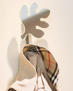 Wieszak firmy Porada w formie liścia, jako dekoracja i przedmiot użytkowy we wnętrzu korytarza, na tle białej ściany. Forma użytkowa, która pełni jednocześnie funkcję dekoracyjną.